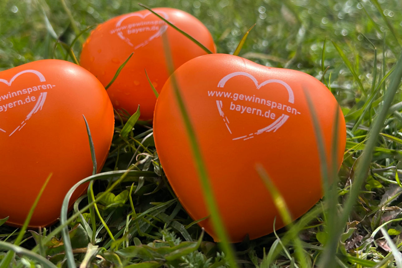 Drei orange Schaumstoffherzen liegen im Gras nebeneinander mit dem Logo des Gewinnsparvereins.