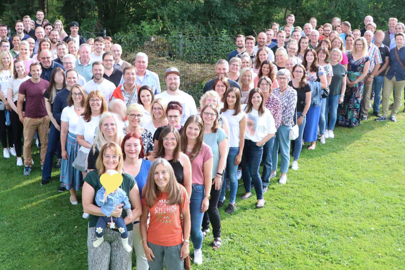 Viele Mitarbeiter unserer Bank stehen auf grünem Rasen als V des Logos aufgestellt.