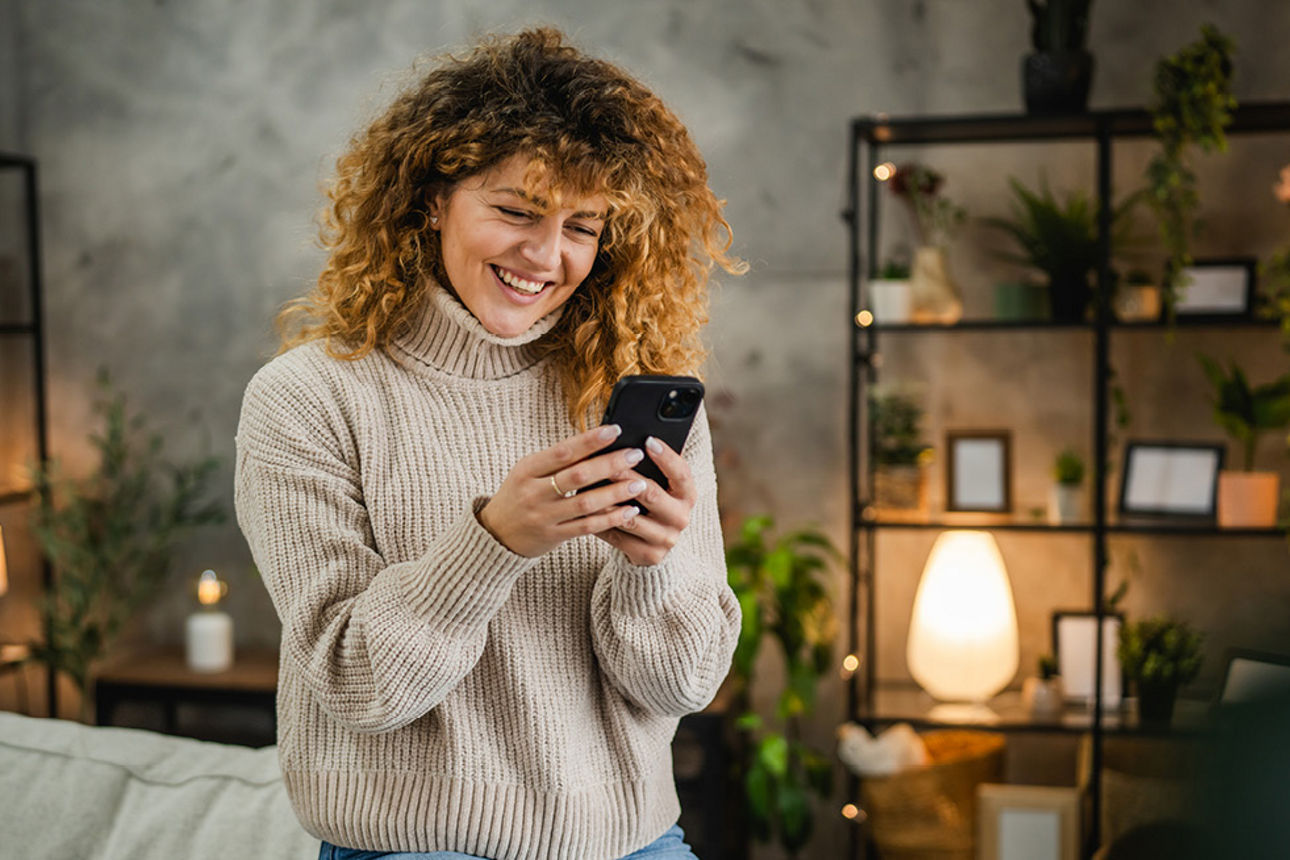 Lächelnde Frau Sitz auf dem Sofa und blickt auf das Smartphone in ihren Händen