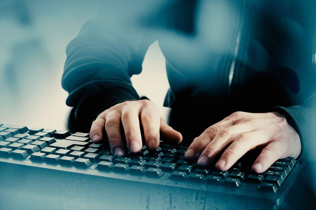 Nahaufnahme von Händen, die auf einer Computer‑Tastatur tippen, aufgenommen in kühler, bläulicher Lichtstimmung.