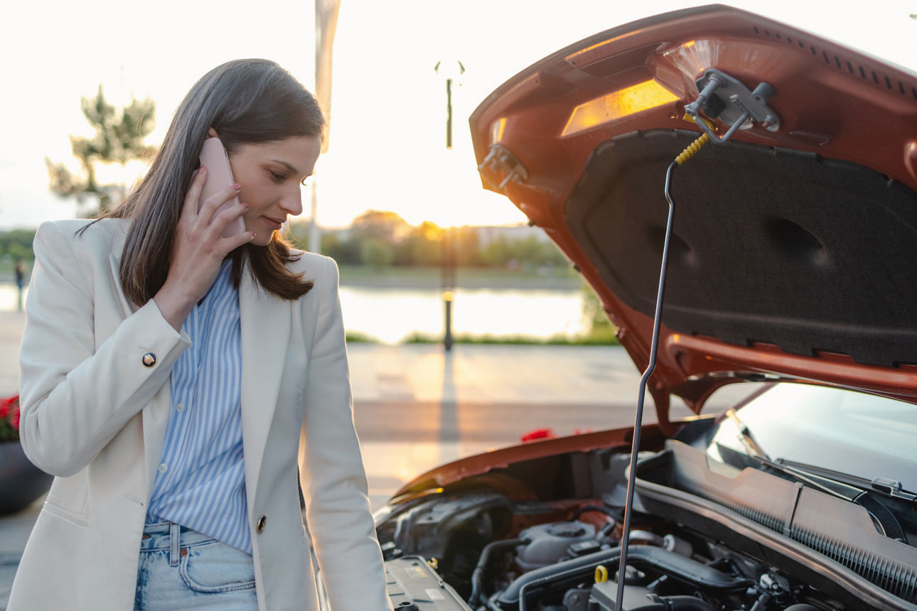 Telefonierende Frau neben Auto mit offener Motorhaube