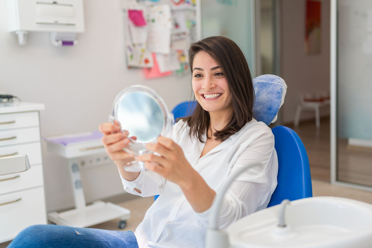 Lächelnde junge Patientin sieht sich im Spiegel an im Zimmer einer Zahnarztpraxis