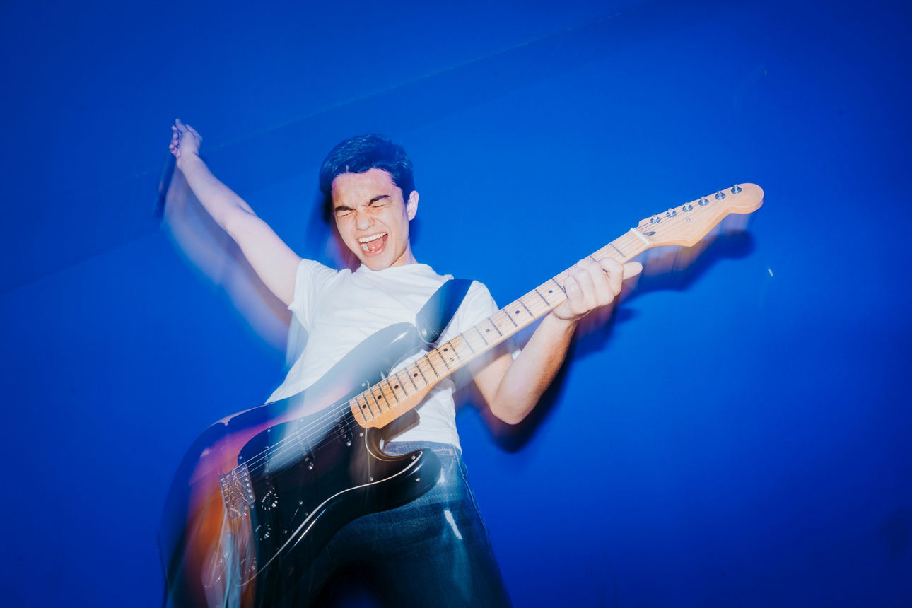 young man with electric guitar on blue background