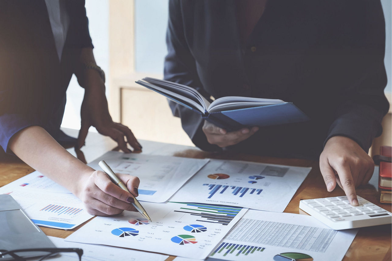 Zwei Personen analysieren Finanzdaten mit Diagrammen, Taschenrechner und Laptop - Symbol für professionelle Vermögensberatung