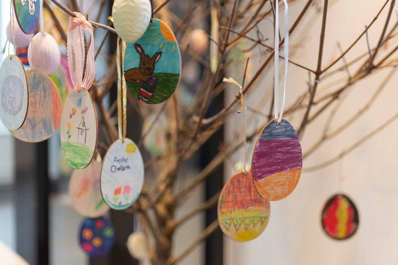 Ein Strauch behangen mit bemalten eierförmigen Holzscheiben.