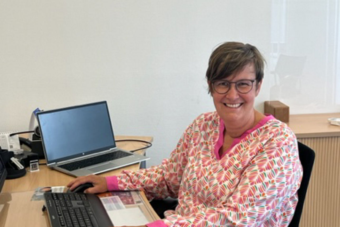 Frau mit Brille sitzt an einer Tastatur an einem Schreibtisch und lächelt