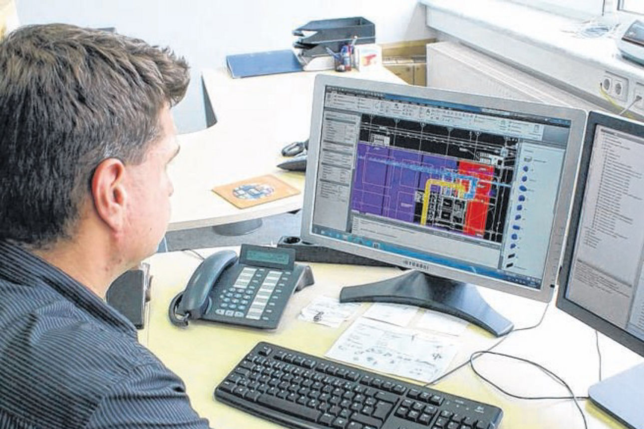 Ein Mann sitzt an einem Schreibtisch und arbeitet an einem Computer, der einen Plan zeigt