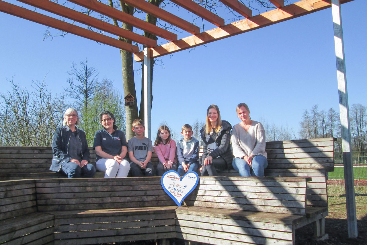 4 Erwachsene und 3 Kinder sitzend beim Scheckübergabetermin 