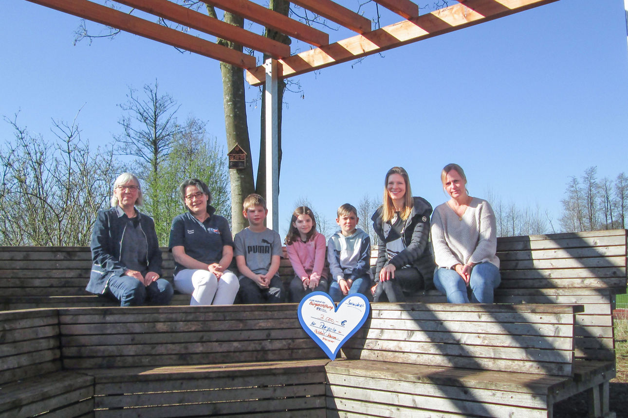 4 Erwachsene und 3 Kinder sitzend beim Scheckübergabetermin 