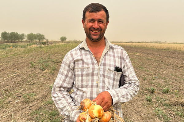 Ein Landwirt aus Tadschikistan steht mit Zwiebeln in der Hand auf einem Feld