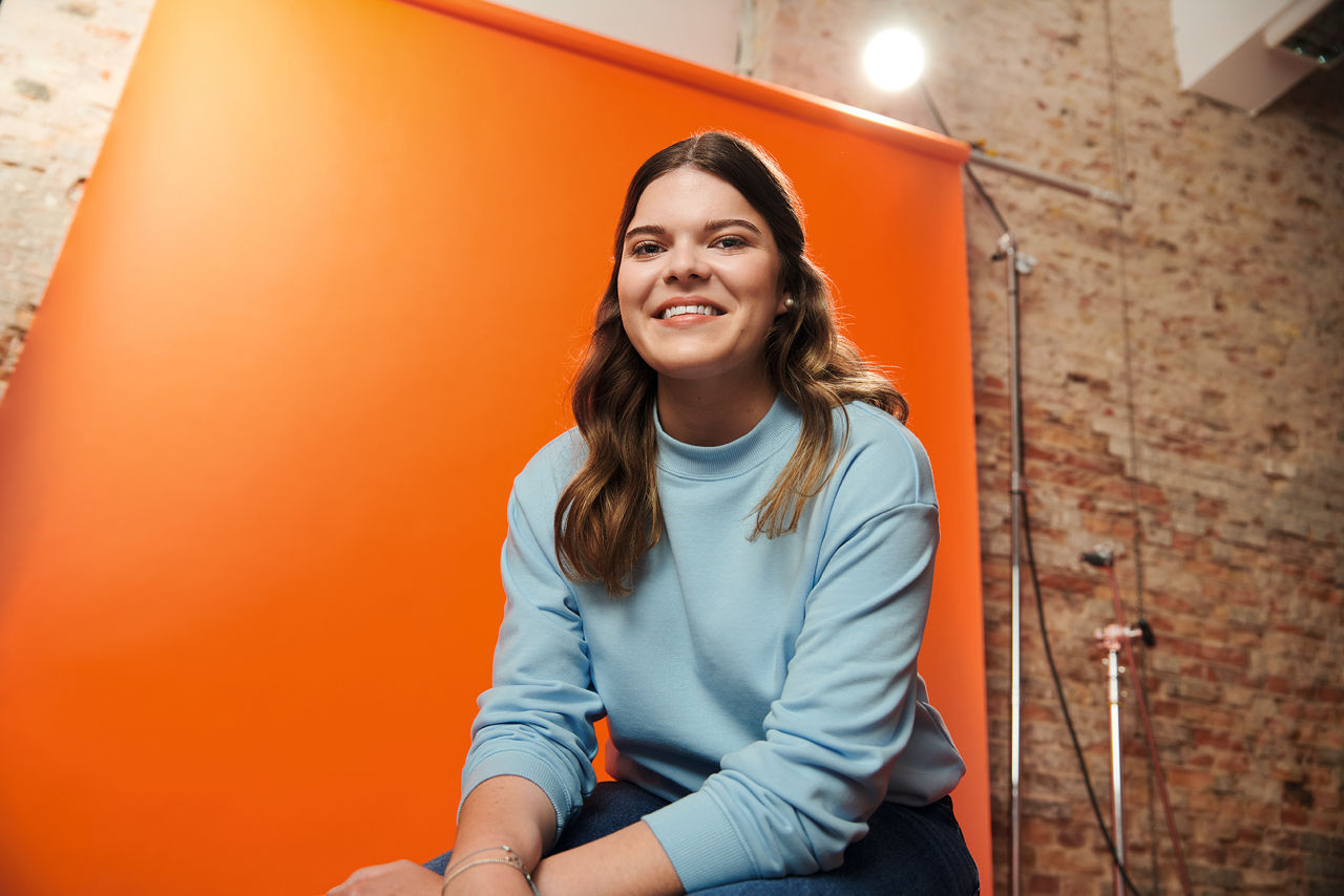 Ein Mädchen sitzt vor einer orange Wand
