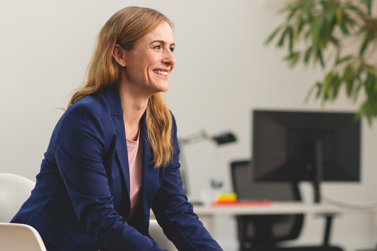 Eine lächelnde Frau sitzt an ihrem Arbeitsplatz