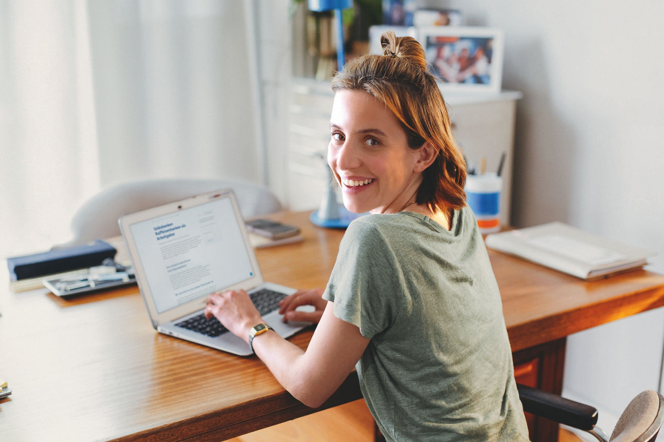 Lächelndes Mädchen sitzt am Schreibtisch und tippt in einen Laptop
