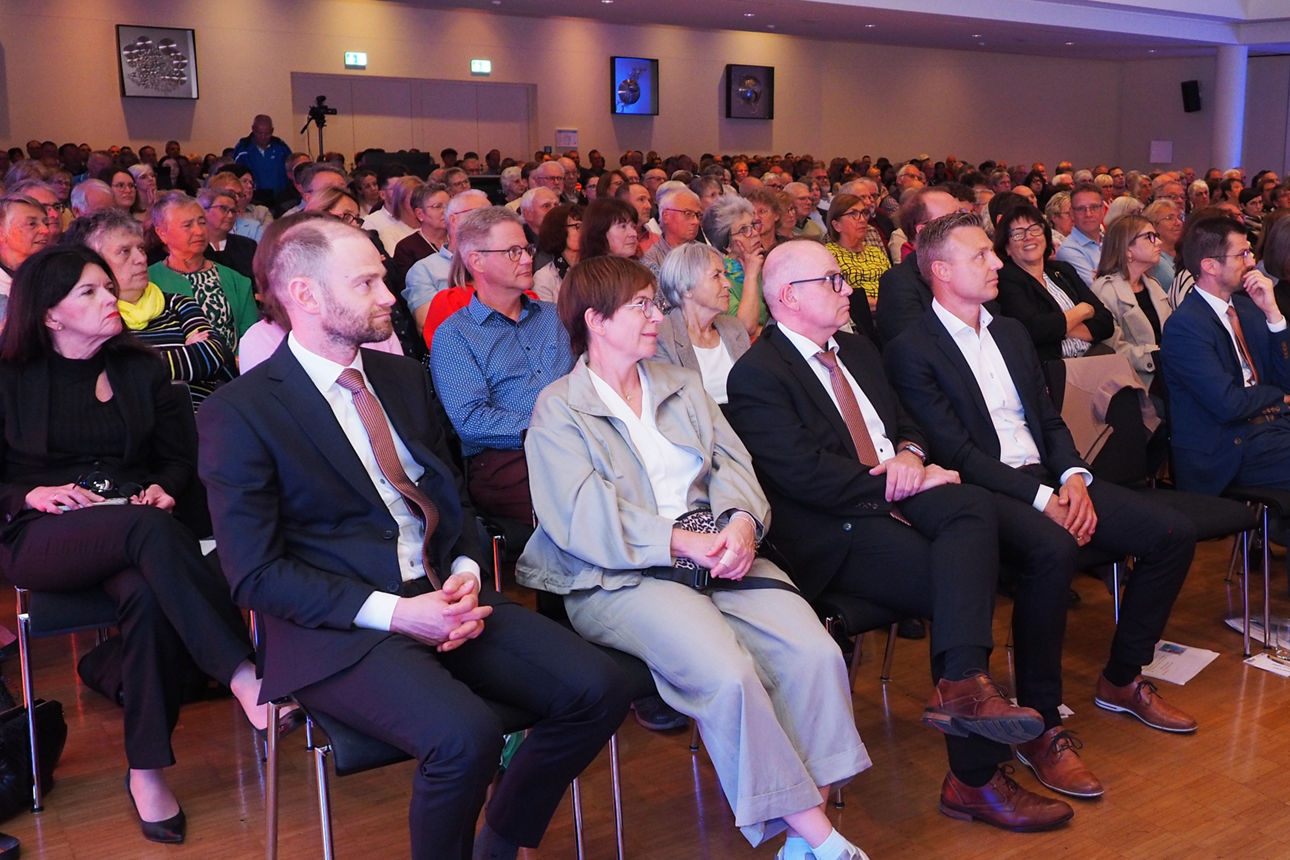 Großes Publikum sitzt in Reihen bei einer Saalveranstaltung.