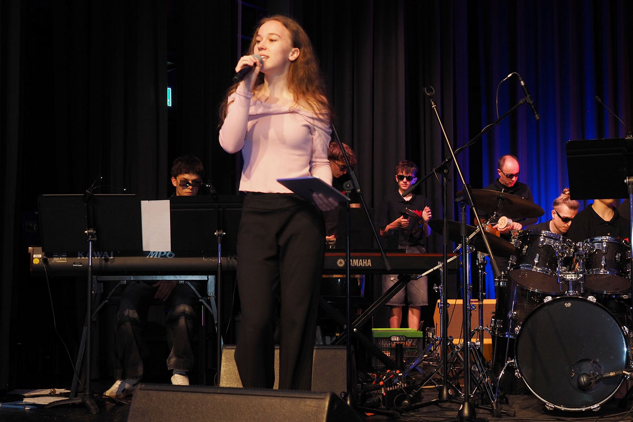 Sängerin auf Bühne mit Band, Keyboard und Schlagzeug, blaues Bühnenlicht.