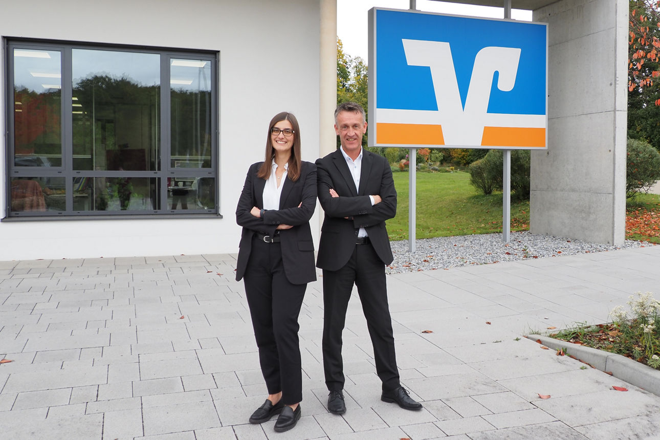 zwei lächelnde Kollegen stehen mit verschrenkten Armen vor unserem Verwaltungsgebäude