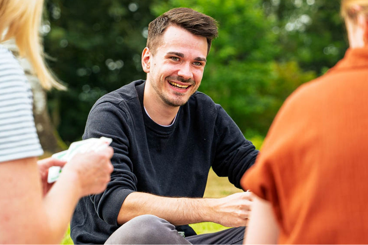 Mann sitzt im grünen und spielt Karten