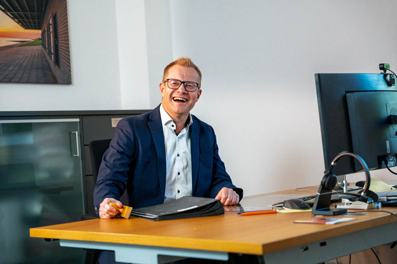 Eine lächelnde Frau mit einem Tablet in der Hand sitzt an ihrem Arbeitsplatz