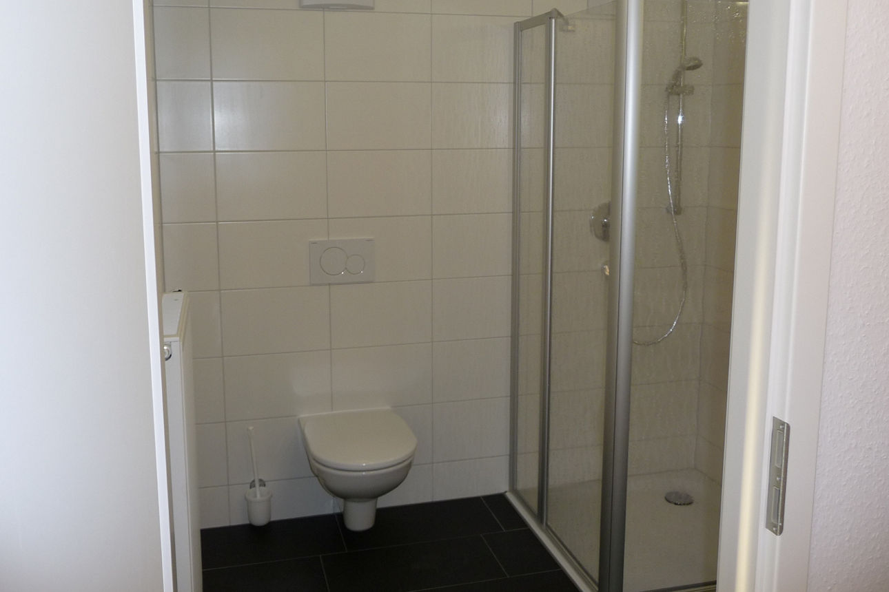 Das Bild zeigt ein beispielhaftes Badezimmer im Studentenwohnheim Wellandstraße. Auf der rechten Seite befindet sich die Dusche, auf der linken Seite befindet sich die Toilette. 
