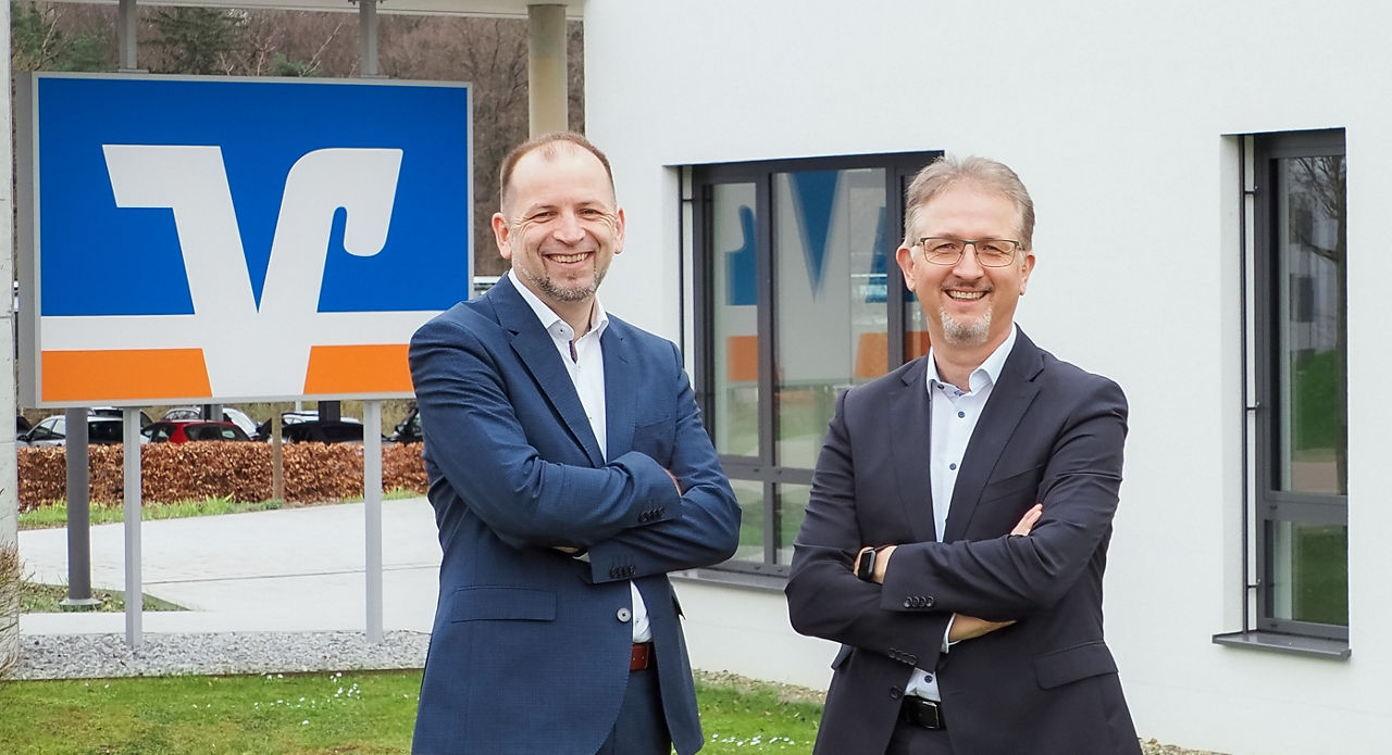Vorstand Bernd Bengel und Roland Gieß stehen vor einem Verwaltungsgebäude 