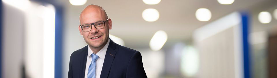 Ein Mann im Anzug und mit Brille lächelt