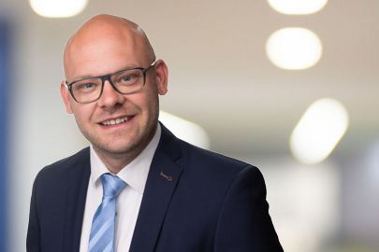 Ein Mann im Anzug und mit Brille lächelt