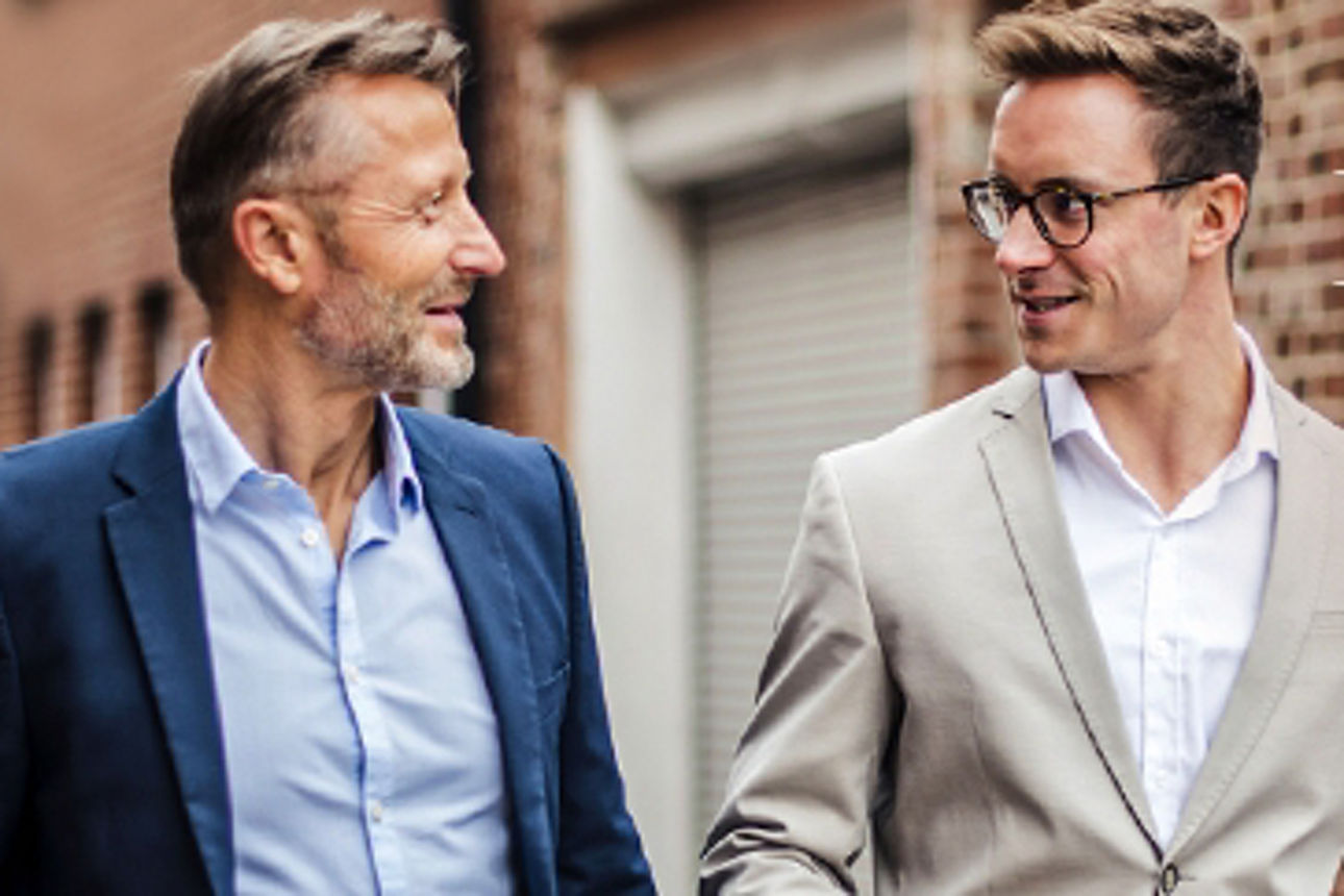 Mann im blauen Anzug läuft neben einem Mann im beige Anzug 