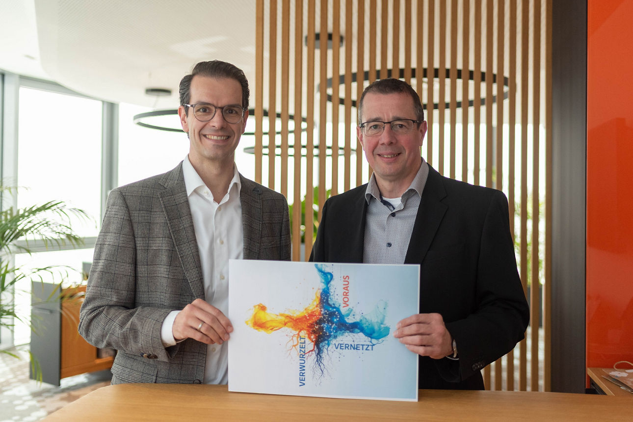 Volksbank Schermbeck Vorstand Stefan Korte und Norbert Scholtholt halten das Motto des Jahres "Verwurzelt - Vernetzt - Voraus" hoch.