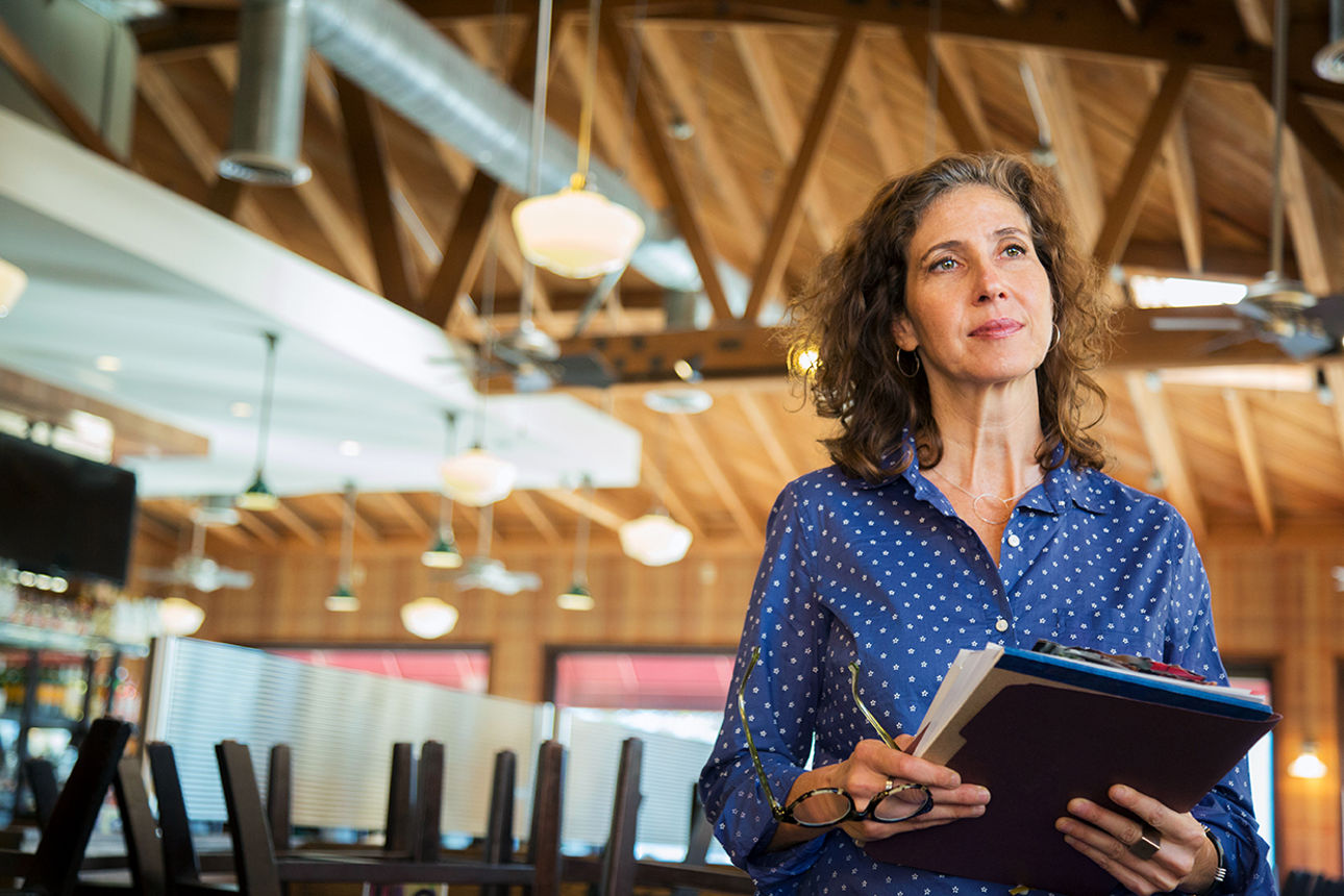 Eine Geschäftsinhaberin steht im Restaurant und hält Unterlagen in der Hand