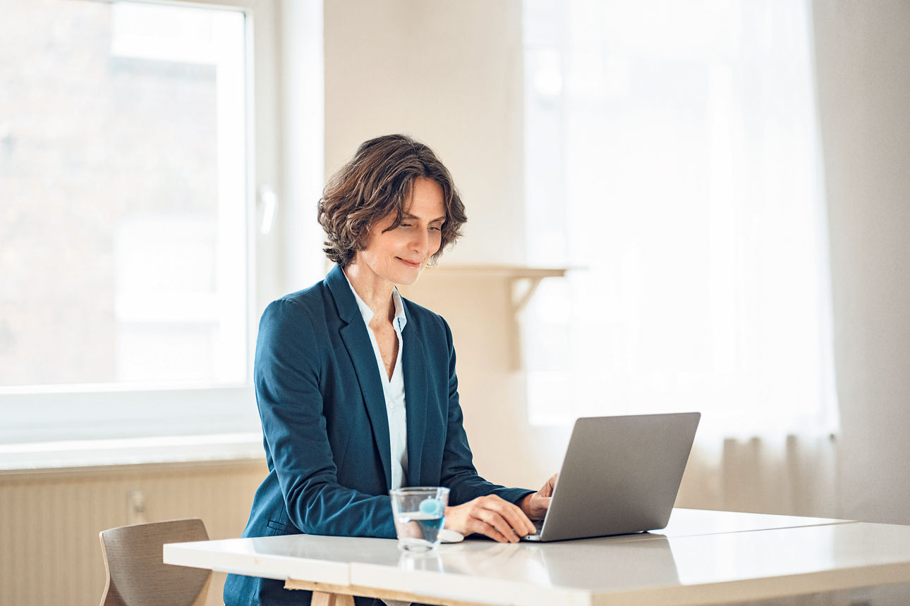 Frau sitzt am Schreibtisch und schreibt auf dem Laptop
