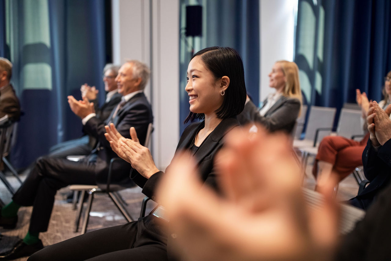 Asian businesswoman sitting with people around clapping hands in auditorium during seminar. Business professionals applauding in a launch event at convention center.