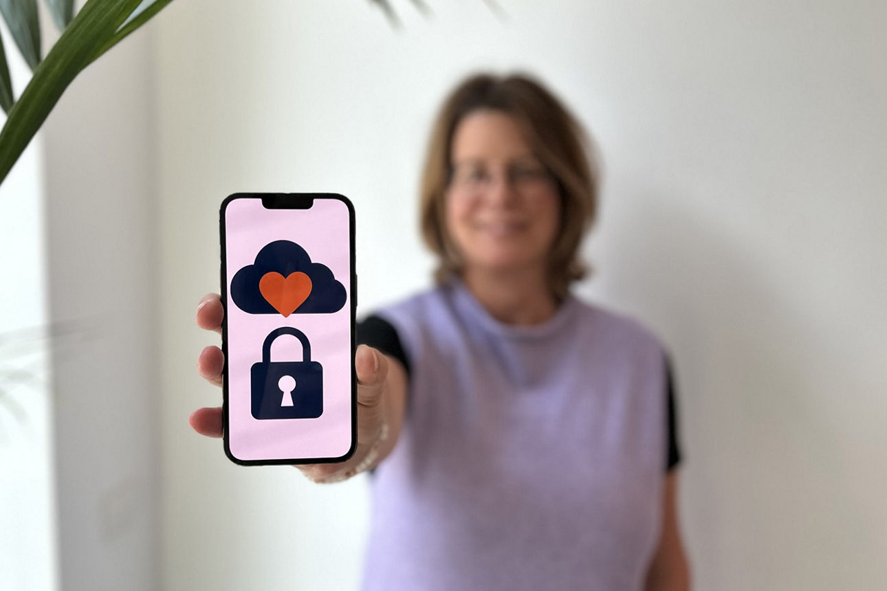 Ein Handy mit den Symbolen einer Wolke, eines roten Herzens und einem Schloss wird von einer Frau in die Kamera gehalten