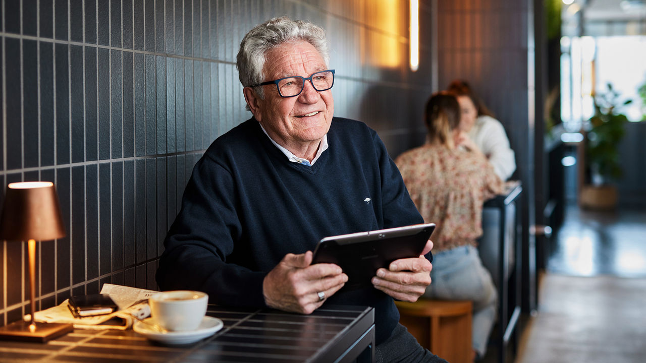 Senior sitz am Tisch und hält in der Hand ein Tablet.