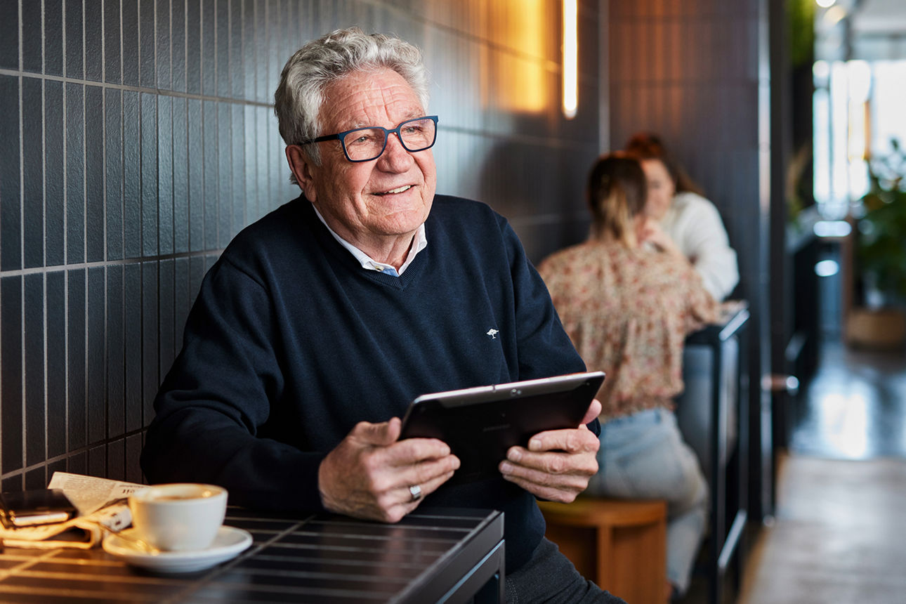 Termin Neukunden - Senior sitzt am Tisch und hält in der Hand ein Tablet
