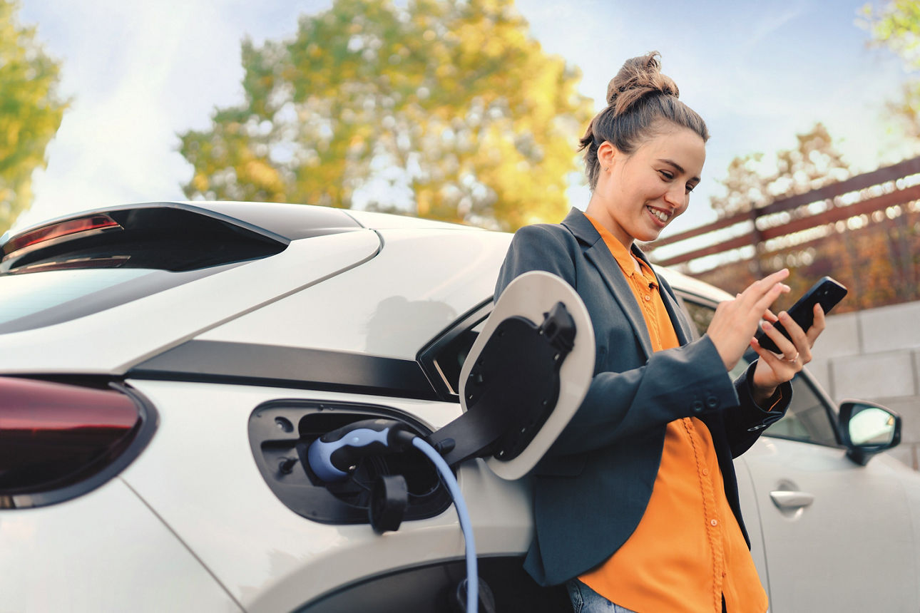 Frau lehnt sich entspannt an einem Auto zurück und schaut auf  ihr Handy