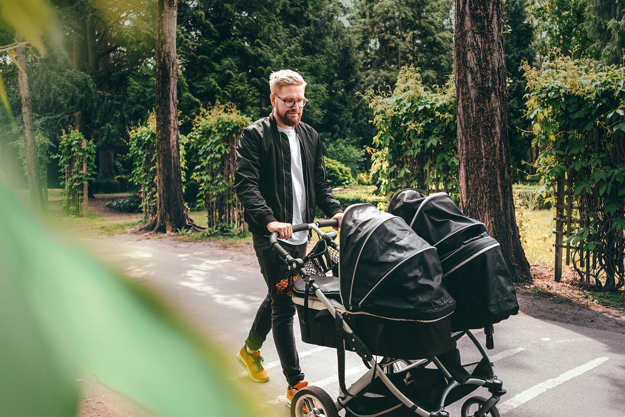 Mann schiebt Kinderwagen mit Zwillingen im Kinderwagen durch einen Park
