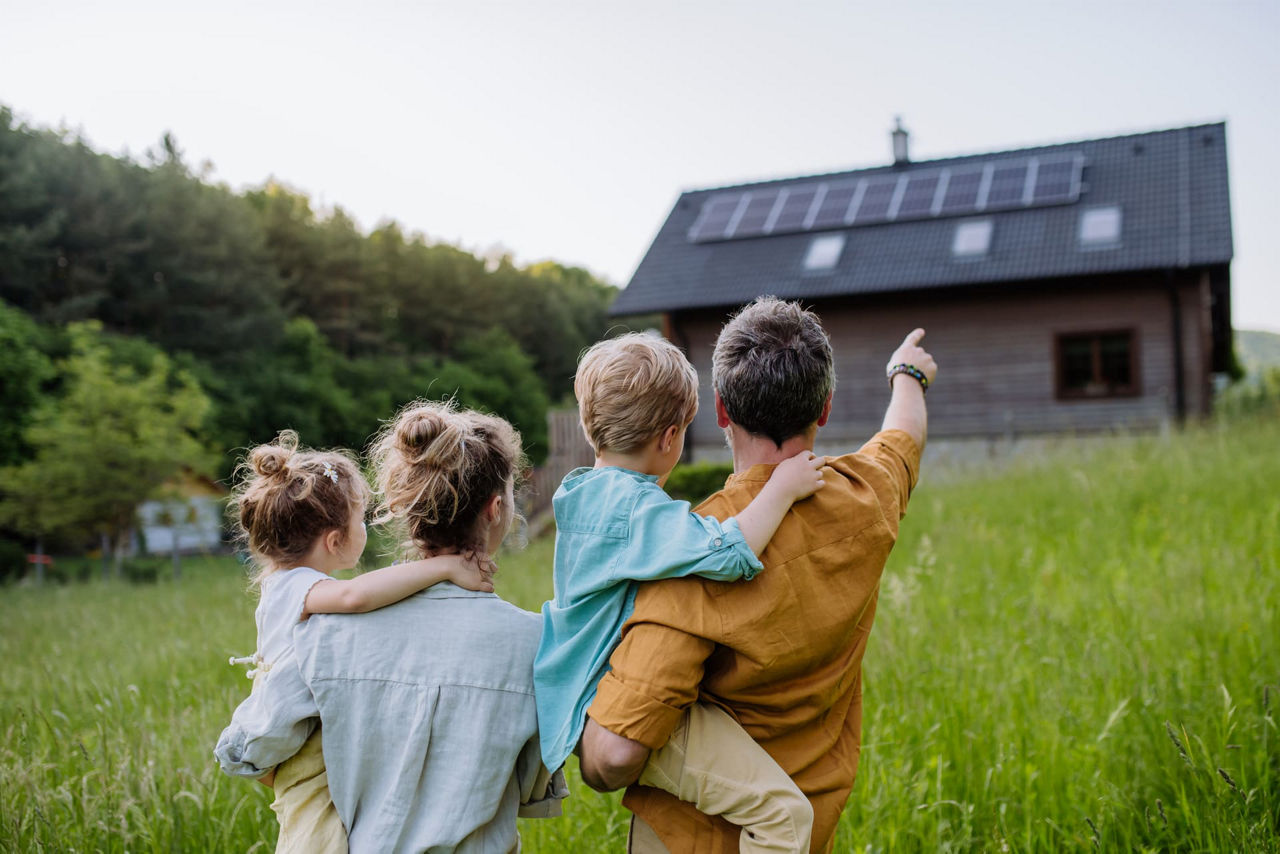 Bild einer jungen Familie, die über eine grüne Wiese geht und auf ihr Haus zuläuft