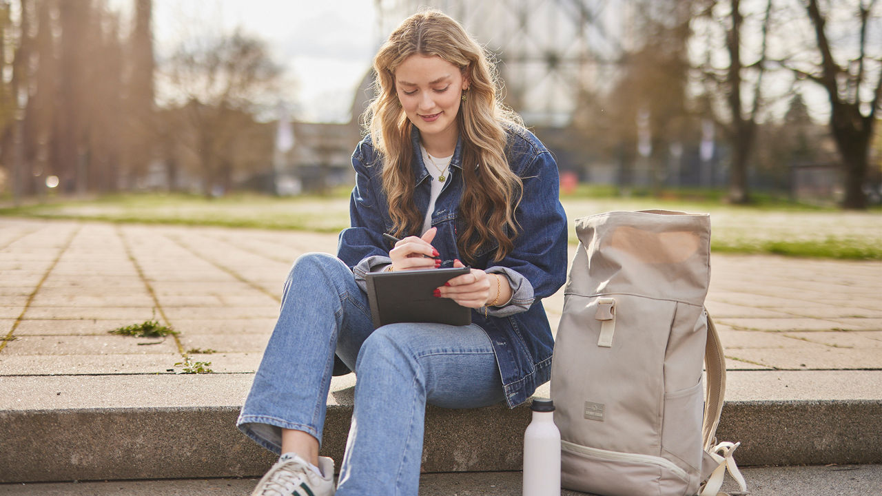 Sitzende Studentin macht sich Notizen auf einer Stufe.