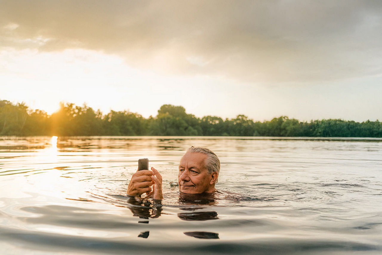Ein älterer Mann mit Smartphone, der in einem See badet. 