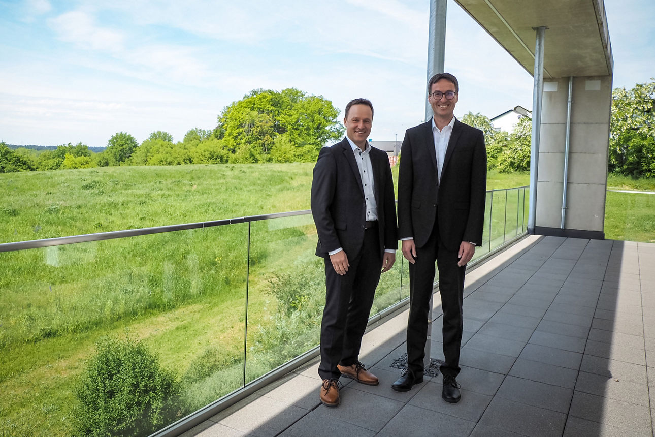 Zwei Männer stehen lächelnd im Grünen