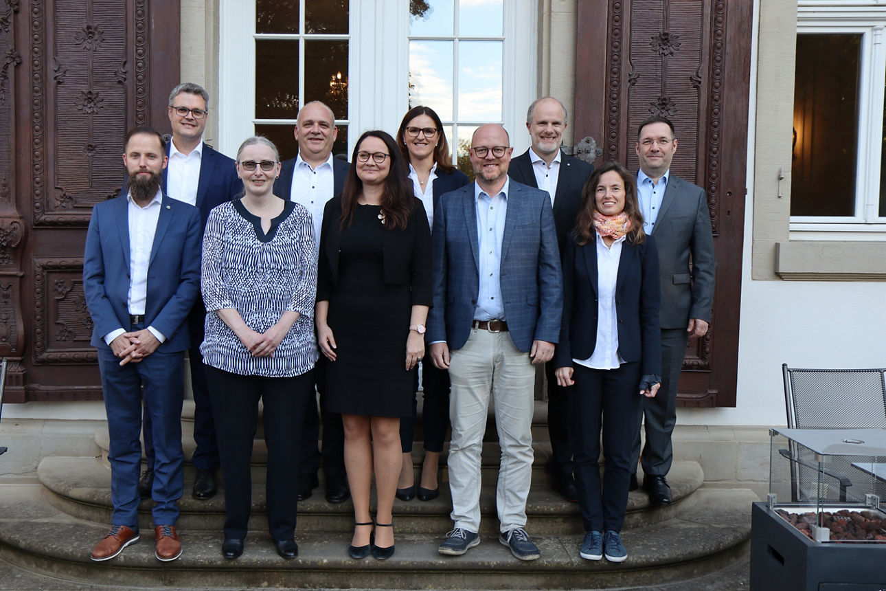 Vor einer Tür stehen auf zwei Stufen zehn Personen, die festlich gekleidet sind 