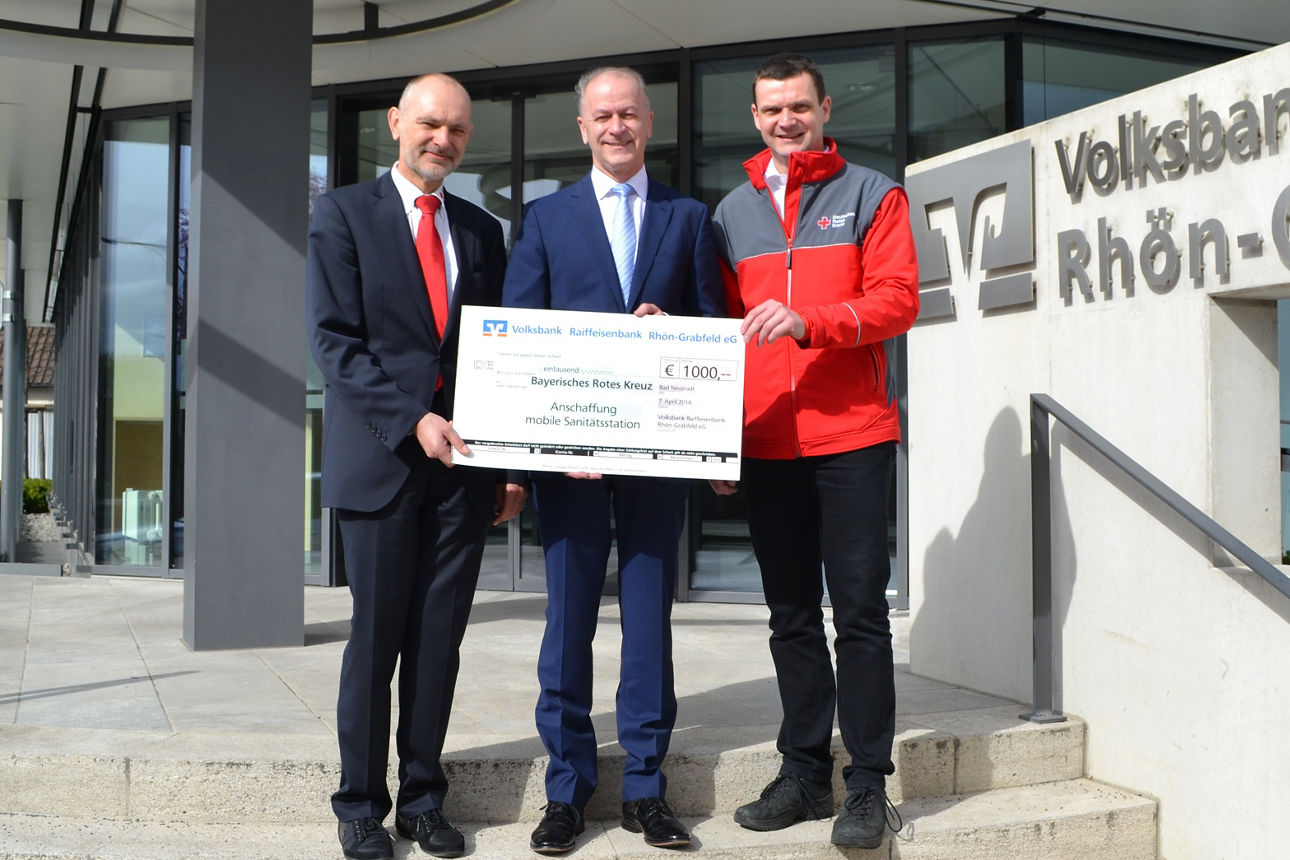 Drei Männer stehen vor einem Bankgebäude und halten einen Spendenscheck in der Hand 