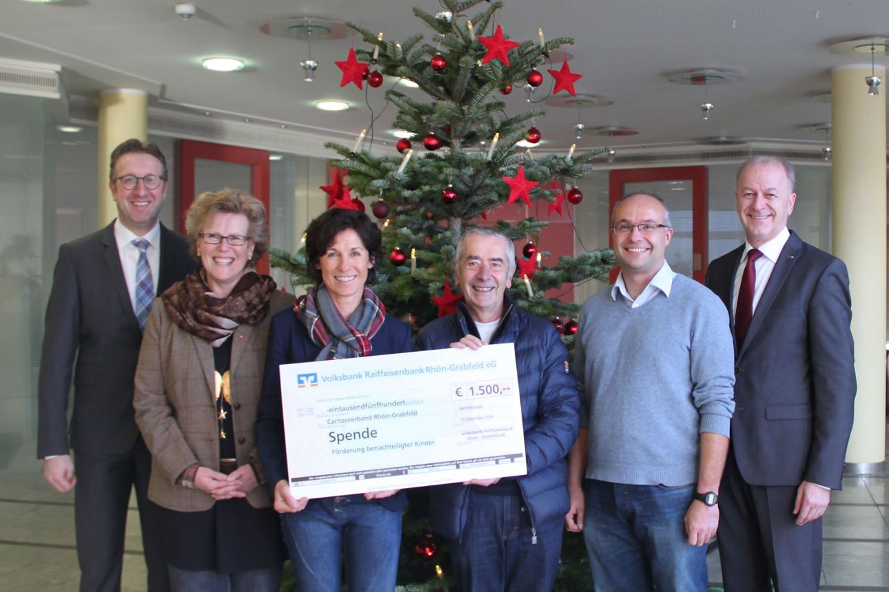 Vier Männer und zwei Frauen stehen vor einem Weihnachtsbaum. Die Frau und der Mann in der Mitte halten einen Scheck