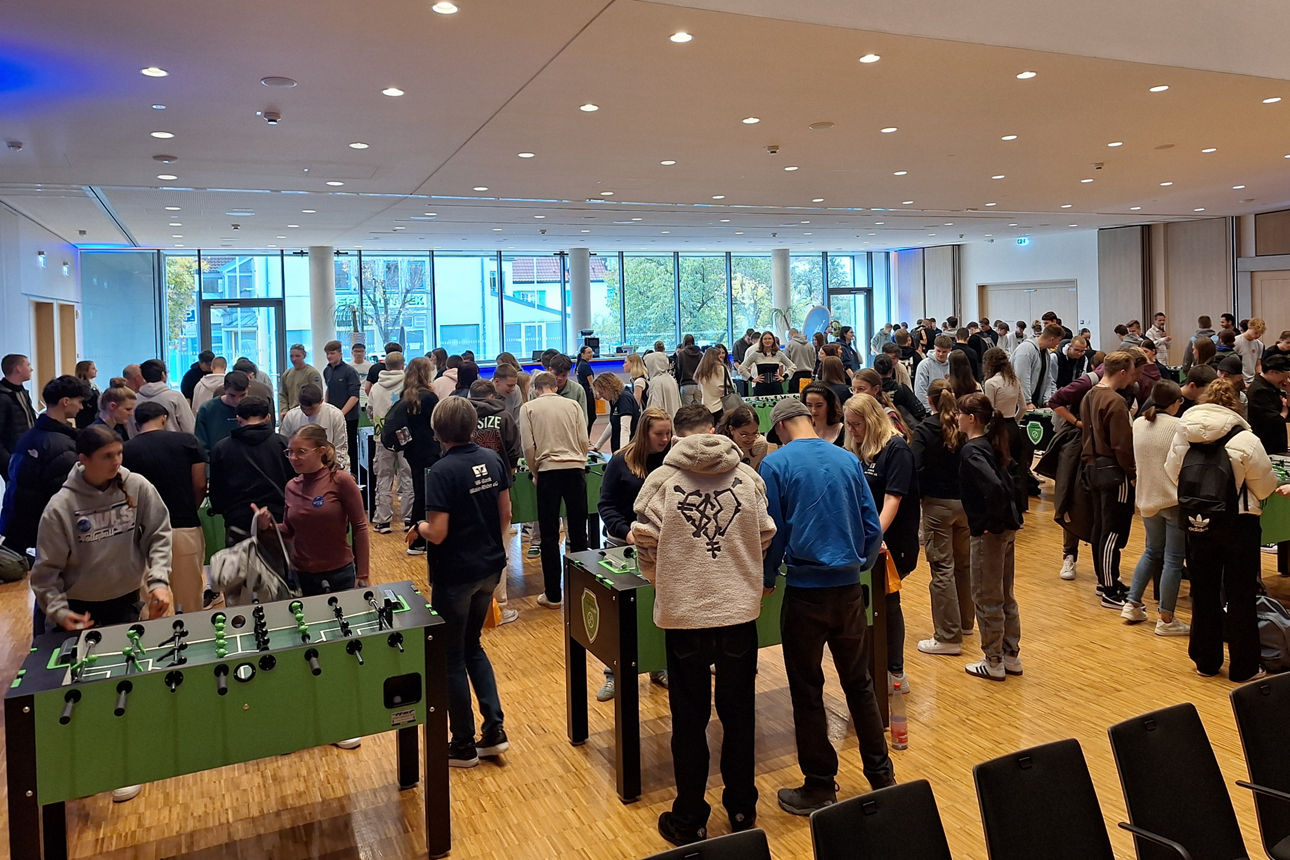 Viele junge Menschen sind in einem großen Raum und spielen an mehreren Kickertischen.