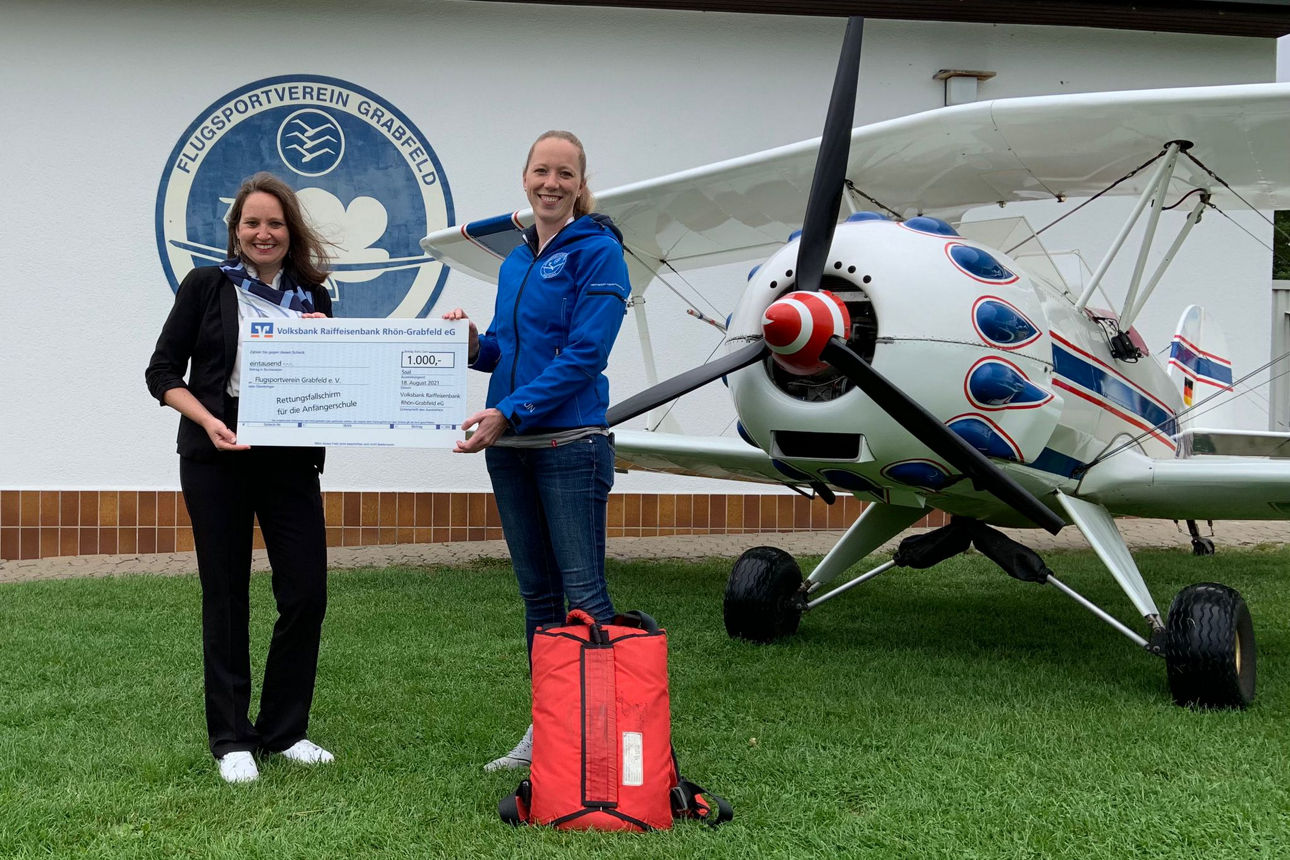 Zwei Frauen stehen auf einer Wiese vor einem Flugzeug und halten einen Spendenscheck in der Hand