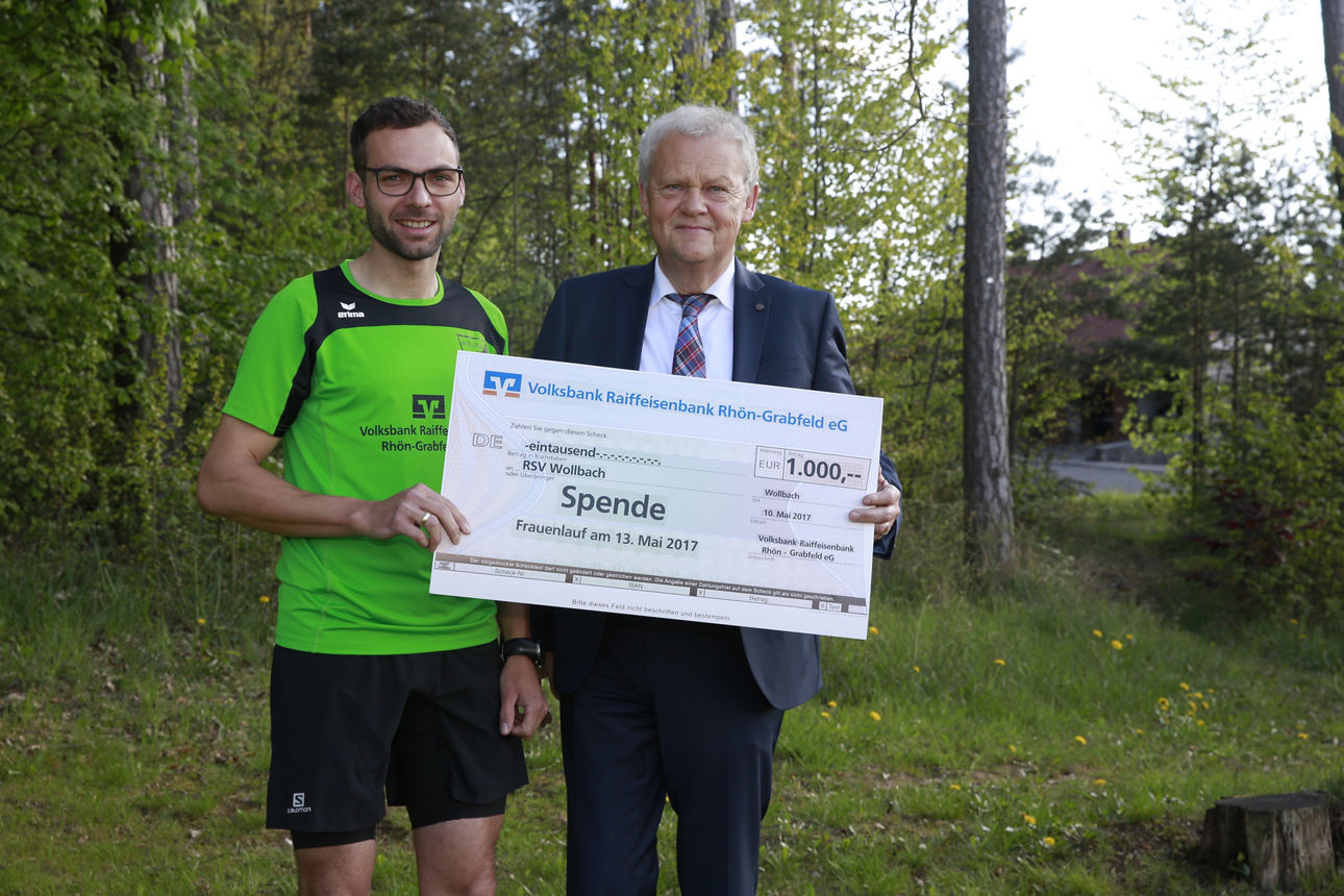 Zwei Männer stehen vor ein paar Bäumen und halten einen Spendenscheck in der Hand 