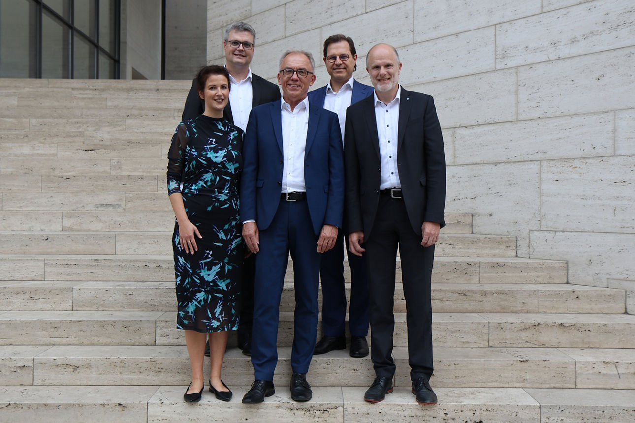 Vier Männer und eine Frau stehen auf einer Treppe und sind festlich gekleidet 