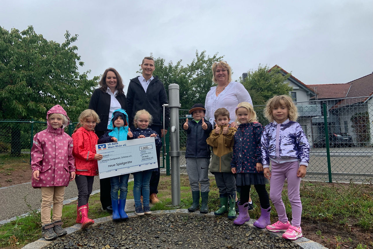 Acht Kinder stehen im Vordergrund dahinter drei Erwachsene, die Kinder auf der linken Seite halten eine Spendenscheck 