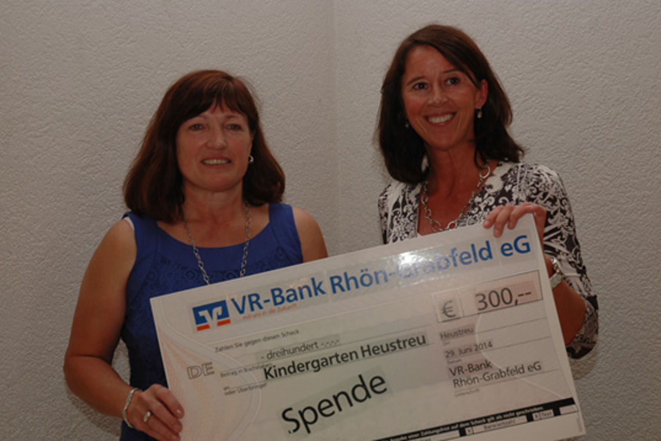 Vor einer weißen Wand stehen zwei Frauen, die einen Spendenscheck in der Hand halten 