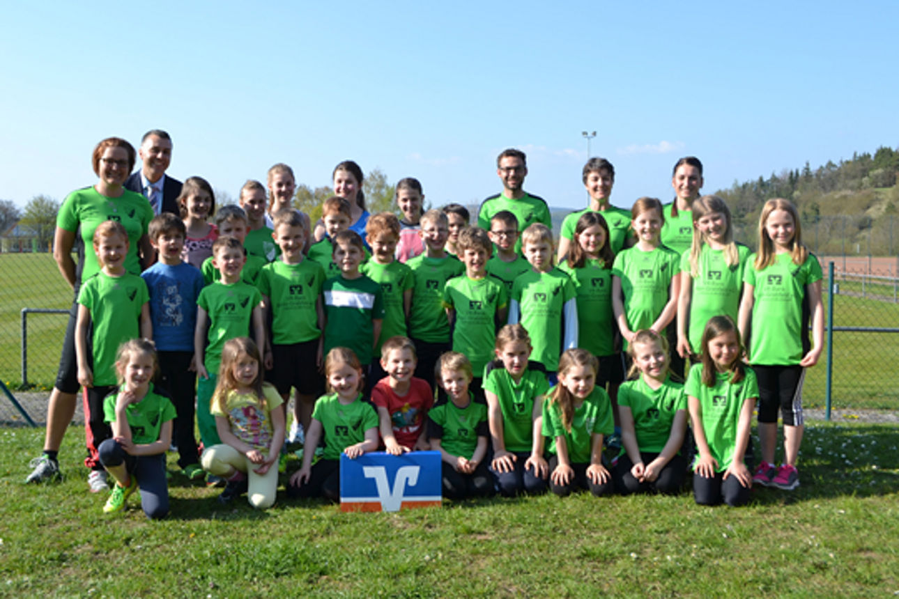 Viele Kinder stehen oder knien auf einer Wiese und tragen grüne Trikots mit dem Logo der VR-Banken